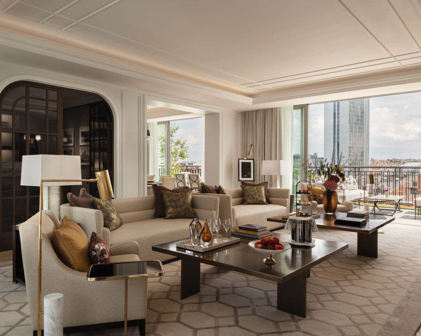 Geräumiges, modernes Wohnzimmer mit Sofas in neutralen Farbtönen, Couchtischen aus Glas, großen Fenstern, Blick auf die Stadt und dekorativen Akzenten auf Tischen und Regalen.