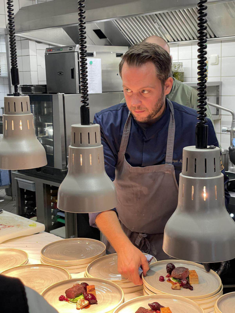 Ein Koch steht in der Küche und beobachtet sein Team bei der Zubereitung der Speisen.
