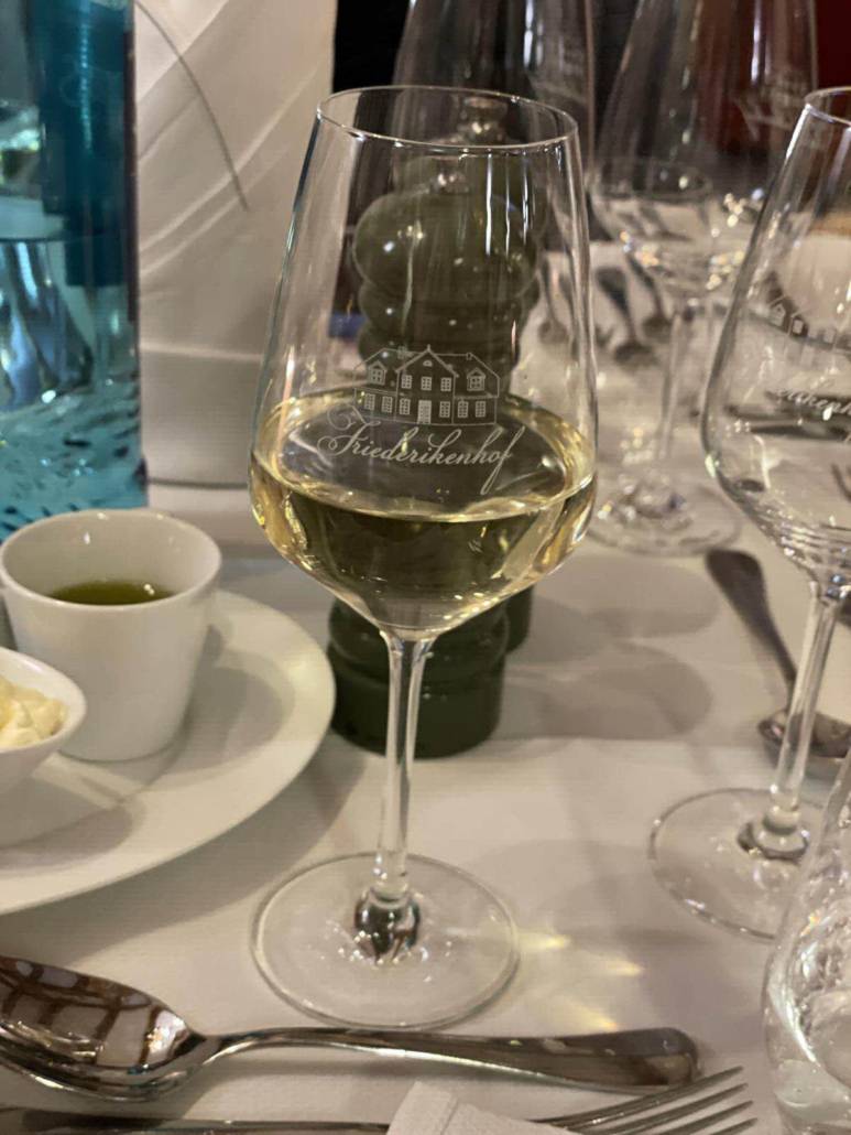 Ein gefülltes Weinglas steht auf einem gedeckten Tisch mit der Aufschrift "Friederikenhof".