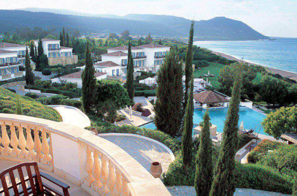 Genießen Sie von Ihrem Balkon im Anassa Resort in Zypern einen atemberaubenden Blick auf weiße Villen, renovierte Zimmer, üppige Gärten, einen glitzernden Pool und die atemberaubende Küstenlinie vor der Kulisse majestätischer Berge.
