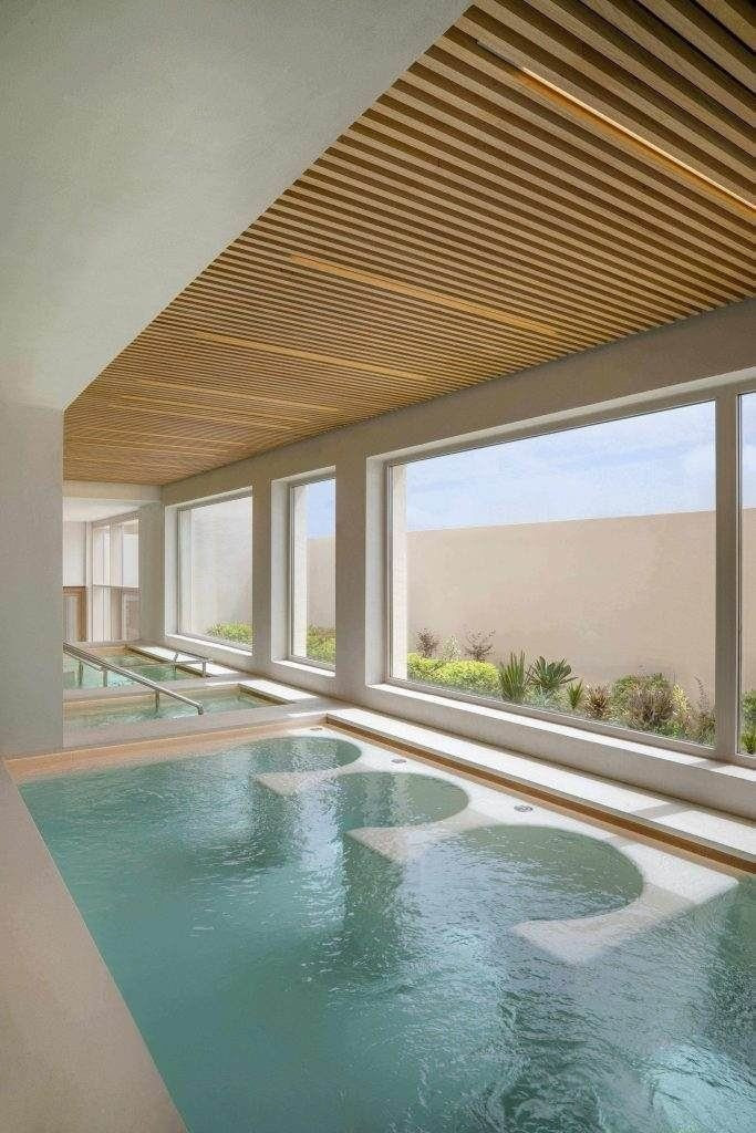 Hallenbad mit eingebauten Whirlpool-Düsen, großen Fenstern, die für natürliches Licht sorgen, und einer Holzlattendecke.