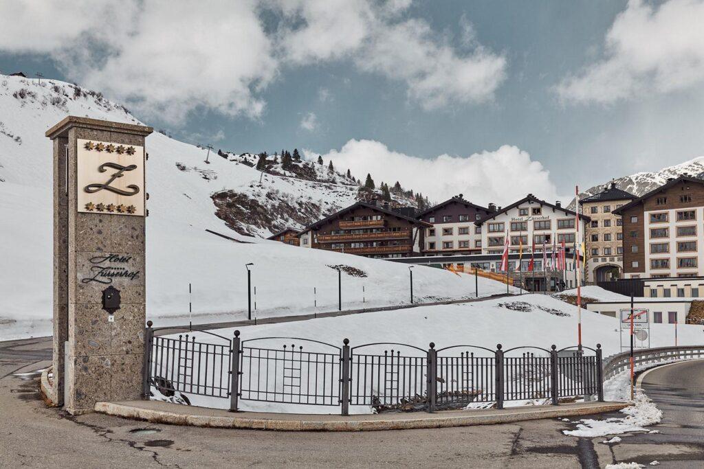 Am Fuße der schneebedeckten Berge liegt ein Hotelkomplex mit mehreren Gebäuden, an dessen Eingang ein steinernes Schild mit der Aufschrift "Z" und mehrere Fahnen angebracht sind.