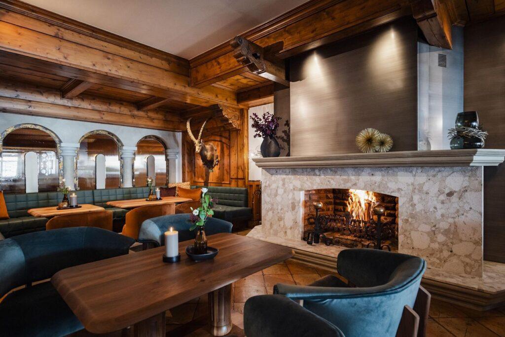 Ein gemütliches Restaurant mit Holzbalken, grün gepolsterten Sitzen, einem beleuchteten Steinkamin, dekorativen Vasen und Tierdekor an der Wand.