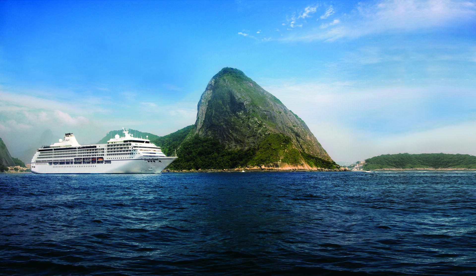 Ein weißes Kreuzfahrtschiff fährt in der Nähe eines großen, steilen Berges an der Küste von Rio de Janeiro in Brasilien unter blauem Himmel.