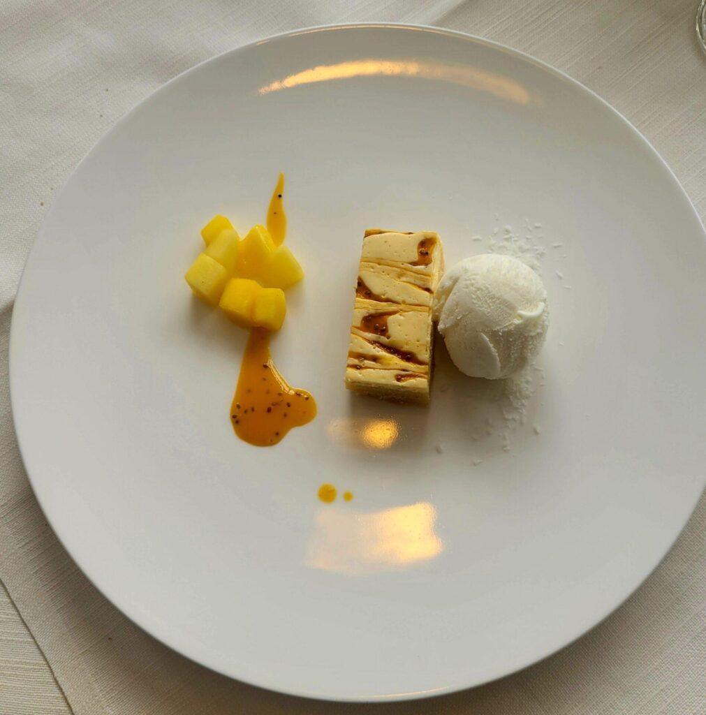 Ein Dessertteller mit Mangowürfeln, einer rechteckigen Scheibe Semifreddo mit Sprühregen und einer Kugel Vanilleeis auf einem weißen Teller.