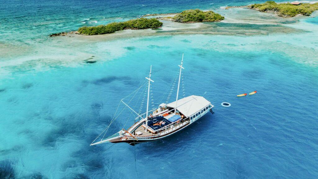 Ein Segelboot ankert im klaren blauen Wasser in der Nähe einer kleinen grünen Insel, in deren Nähe ein Kajak und ein Schlauchboot schwimmen.